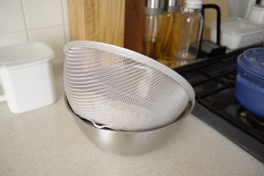 ボウルの縁に丸ざるの足を引っ掛けて米とぎ後の水切りをしている写真